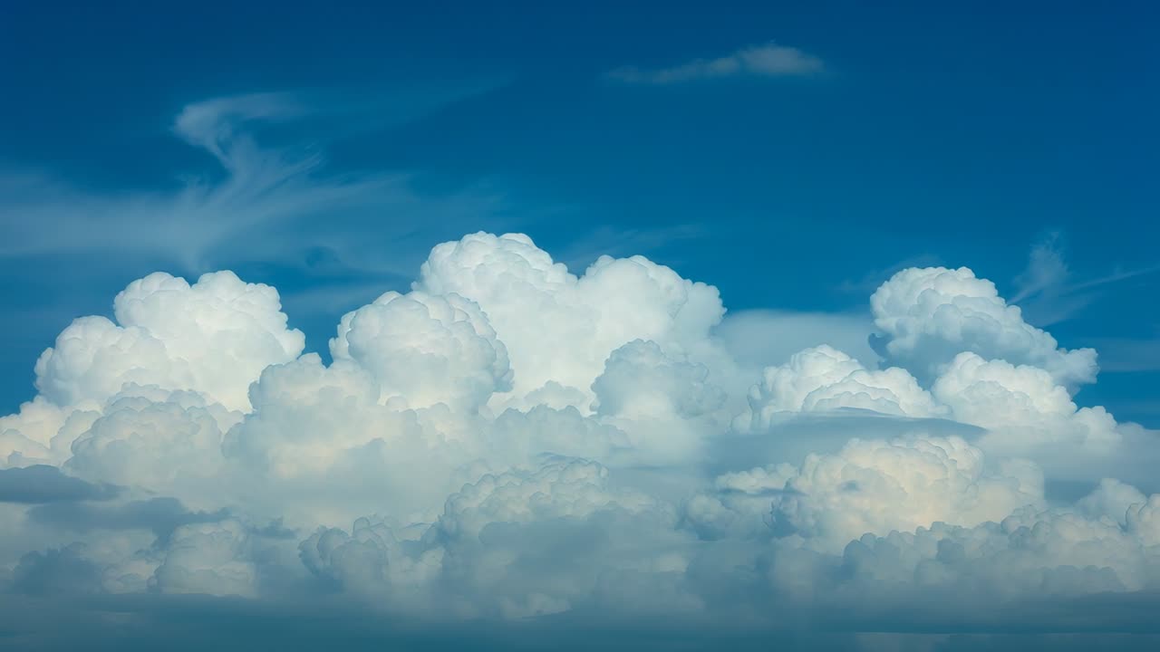 Growing cumulus formation merging under high-altitude winds in blue sky, with cirrus clouds
