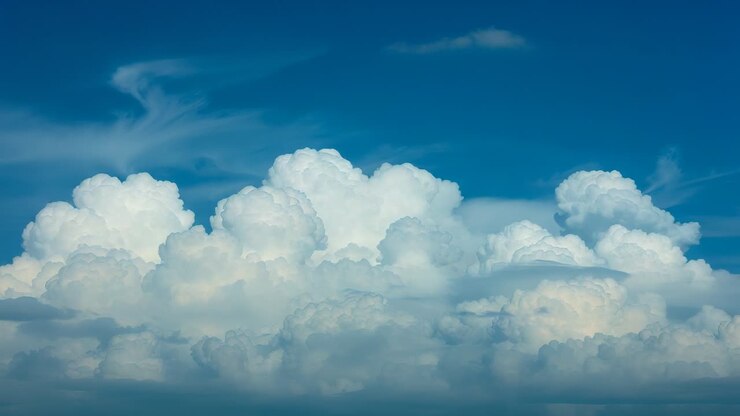 Growing cumulus formation merging under high-altitude winds in blue sky, with cirrus clouds