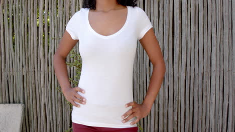 sección media de una mujer biracial en camiseta blanca con las manos en las caderas al aire libre, espacio de copia, cámara lenta