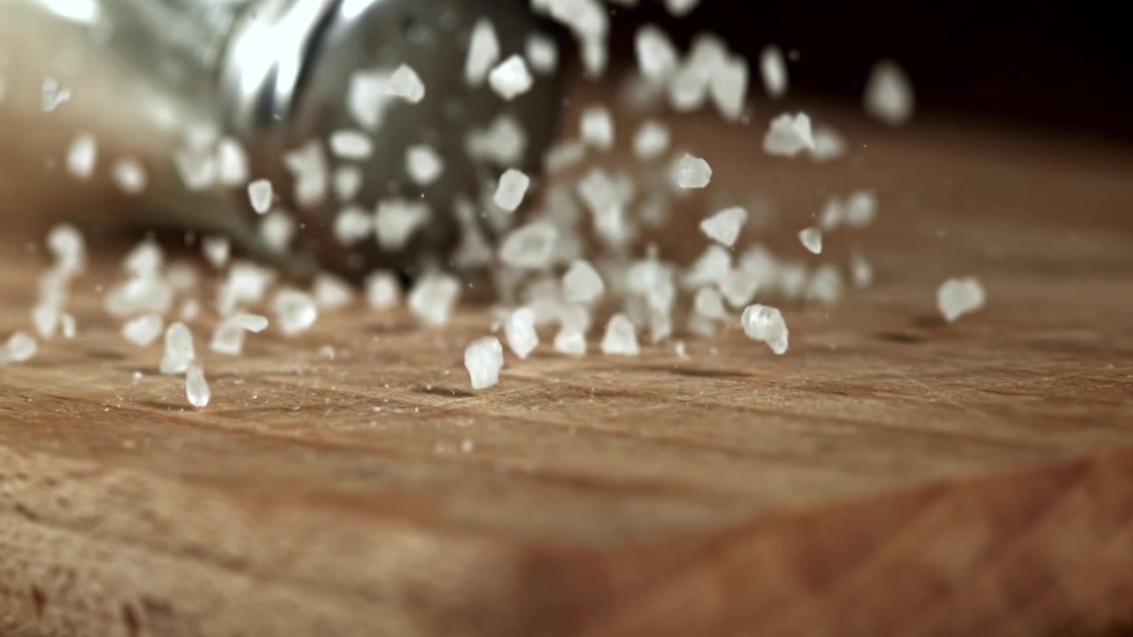 Primo piano al rallentatore di sale grosso che cade su un tagliere di legno.