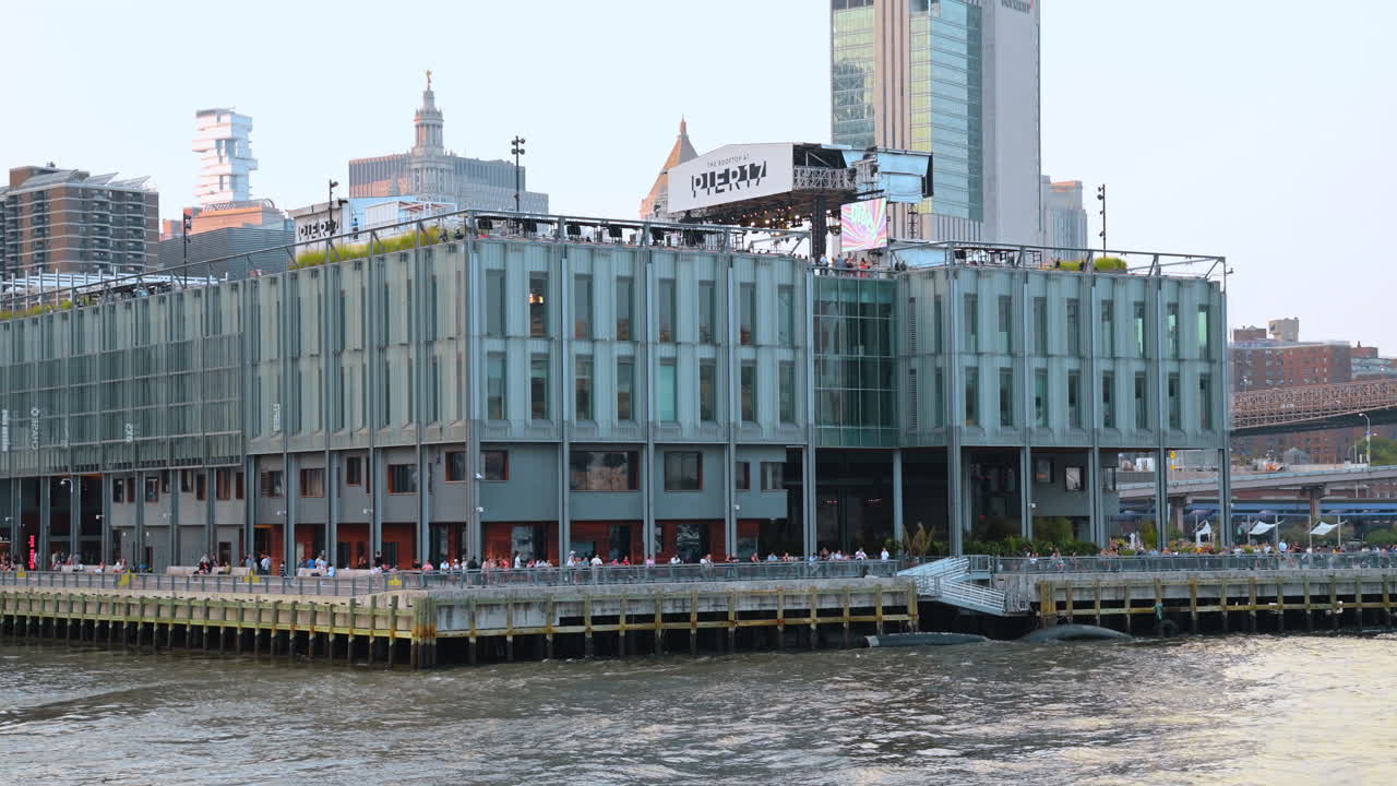 New York, USA, 9 tháng 8 năm 2025: Tòa nhà hiện đại tại bến cảng với tầm nhìn đường chân trời thành phố. Khu phức hợp giải trí Pier 17 trên sông East River với Cầu Brooklyn hiện rõ ở hậu cảnh.
