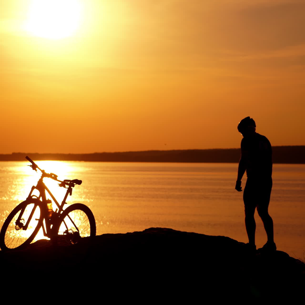Sports bike and bicyclist at sunset near the river. Amazing view of golden path over the water surface on the bike and a silhouette of a man outdoors.