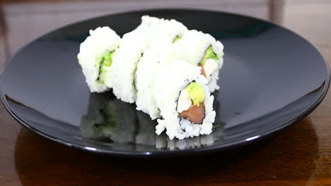 this is a video of sushi on a black plate with a hand and chop sticks picking up a piece