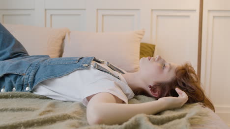 천장을 바라보며 침대에 누워 있는 사려 깊은 소녀가 옆으로 돌아서 카메라를 쳐다본다