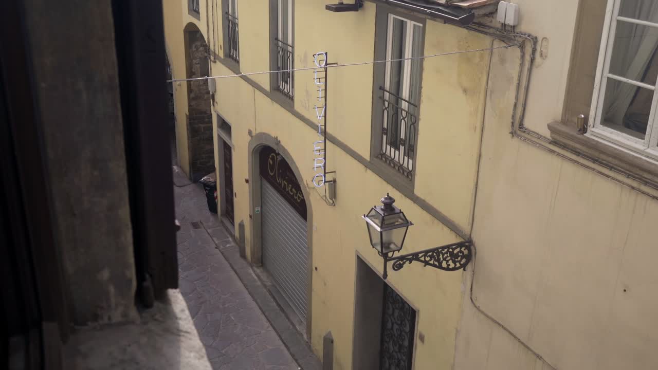 A view looking down into a narrow alleyway in Florence, Italy, featuring a vintage street lantern mounted on a building.
