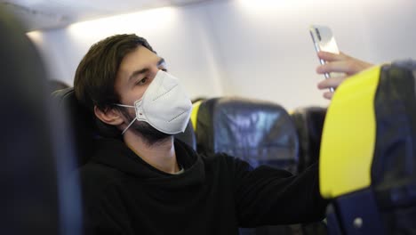 hombre con máscara respiratoria viajando en un avión durante tiempos de pandemia toma una selfie