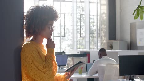 thoughtful biracial casual businesswoman using tablet in sunny office, copy space, slow motion