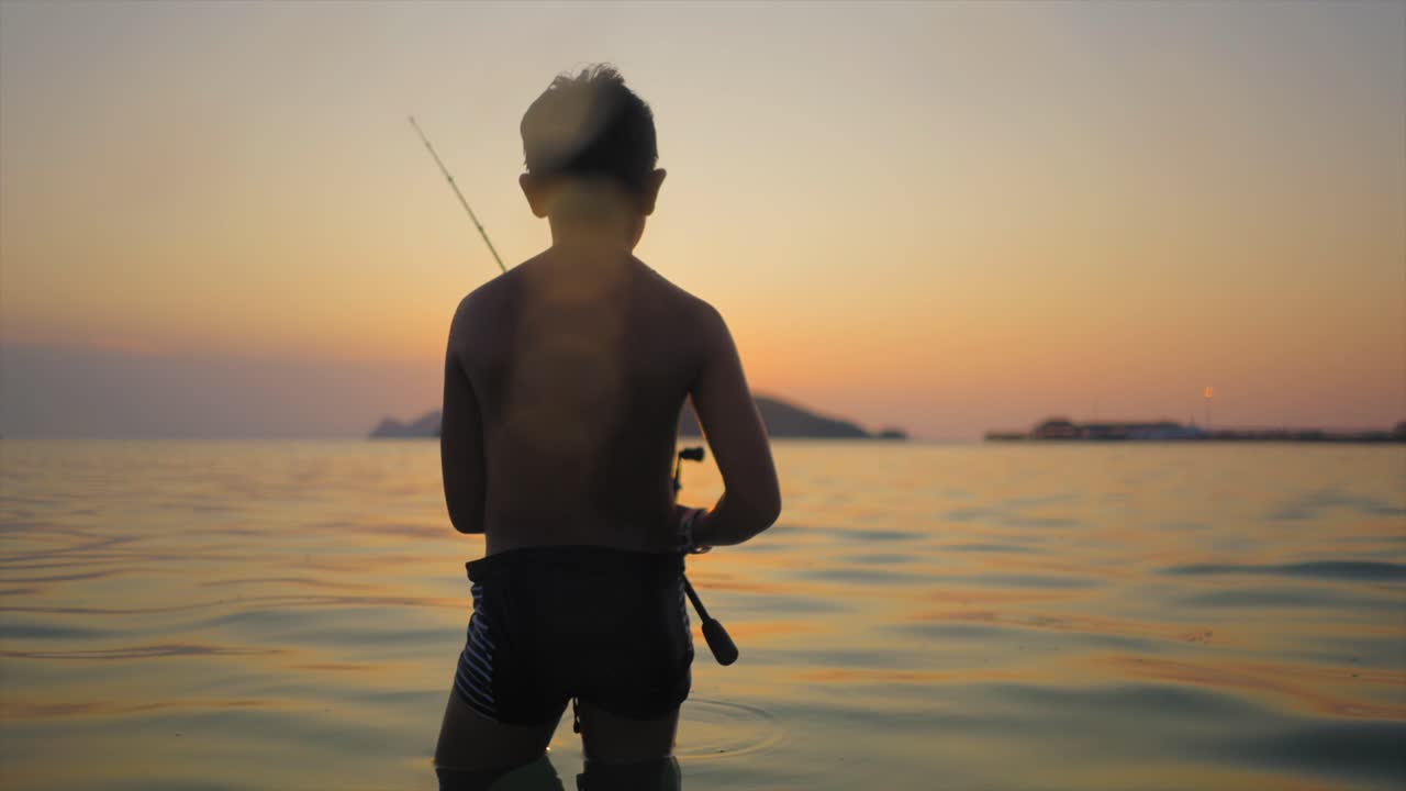 Silhouette of a young boy fishing in the sea at sunset