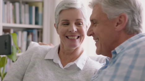 Feliz-Pareja-De-Ancianos-Teniendo-Video-Chat-Usando-Un-Teléfono-Inteligente-Saludando-A-Sus-Nietos-Disfrutando-Charlando-Con-Su-Familia-Por-Teléfono-Móvil-Compartiendo-Su-Estilo-De-Vida-Relajándose-En-Casa-Al-Jubilarse-4k