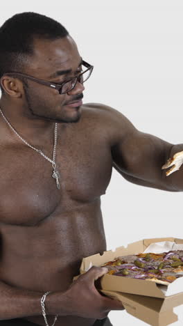 african american man eating pizza. black muscular man enjoying delicious pizza from carton package. sportsman eats unhealthy food isolated in studio. slow motion. vertical video