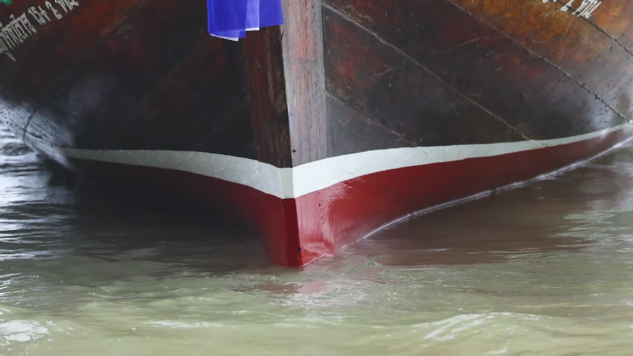 Detailed view of a wooden boat's bow cutting through water, showcasing traditional craftsmanship and movement.
