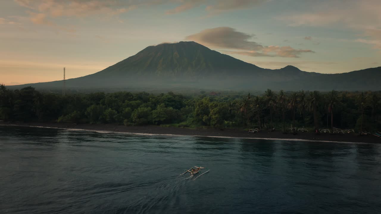 Fishing boat arriving at moody tropical shore of Bali with grand Mount Agung, Kubu Beach, aerial