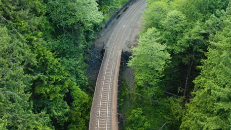 empty railroad tracks in middle of lush green forest with no train, gradual pan up aerial drone shot