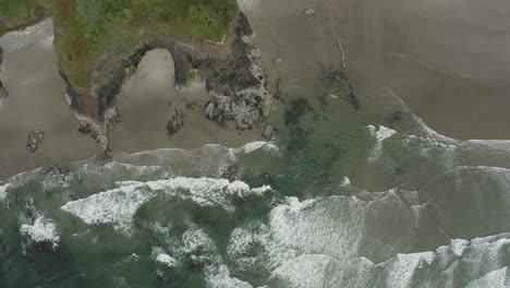 Toma-Fija-De-Drones-Aéreos-De-Olas-Que-Entran-En-Acantilados-Rocosos-Y-Playa-De-Arena,-Costa-De-Oregon