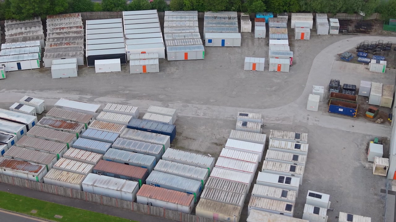 File di container di spedizione immagazzinati in un deposito industriale. Pile organizzate di container di carico in acciaio. Scorte in eccesso, gestione della logistica, soluzioni di stoccaggio industriale su vasta scala. Vista aerea. Regno Unito