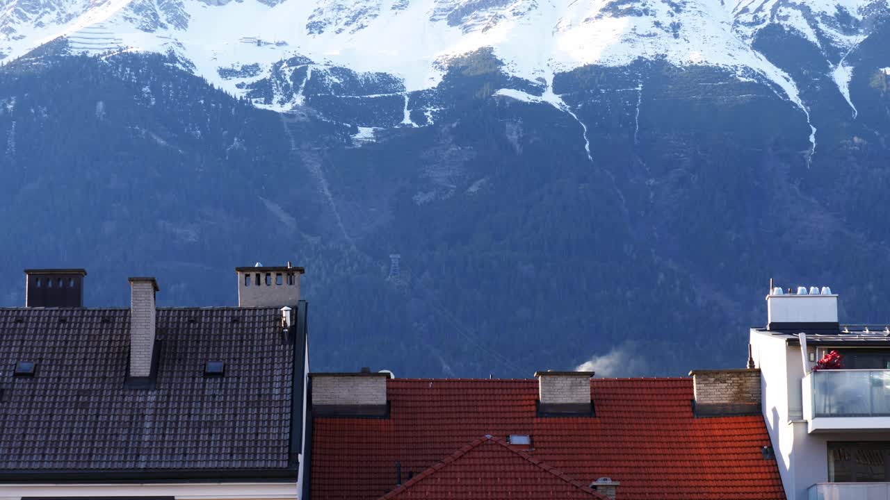 humo que se eleva de la chimenea de la casa en el invierno frío, quema crisis de energía de calefacción, montaña nevada en el fondo
