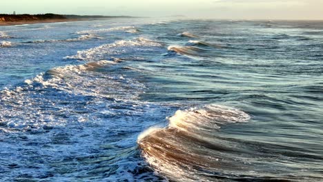 Rugged-waves-cresting-along-a-vast-beachfront,-The-dynamic-interface-of-sea-and-land-under-the-open-sky