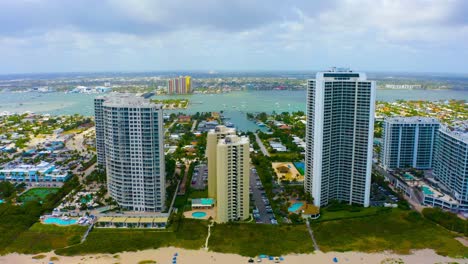 un dron aéreo disparado se eleva lentamente sobre la playa en la isla singer mirando hacia altos edificios residenciales en west palm beach, florida en un día de cielo azul