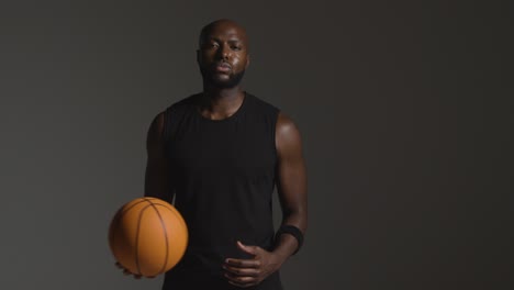 retrato de estudio de un jugador de baloncesto que sostiene la pelota bajo el brazo contra un fondo oscuro 1