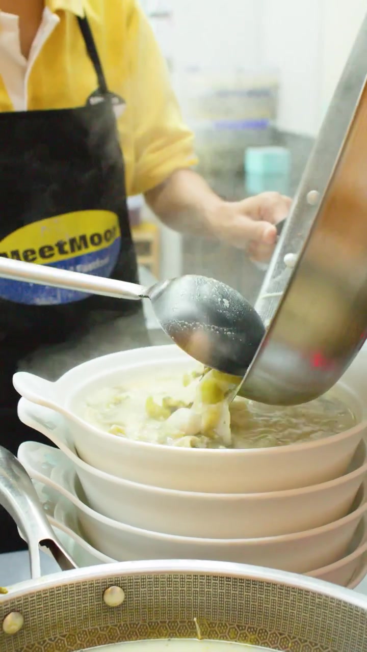 Professional chef pours steaming broth from a large wok into stacked white ceramic bowls.