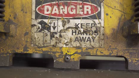 close up shot of an automated metal shear, cutting steel, inside a industrial factory, with a danger sign on it