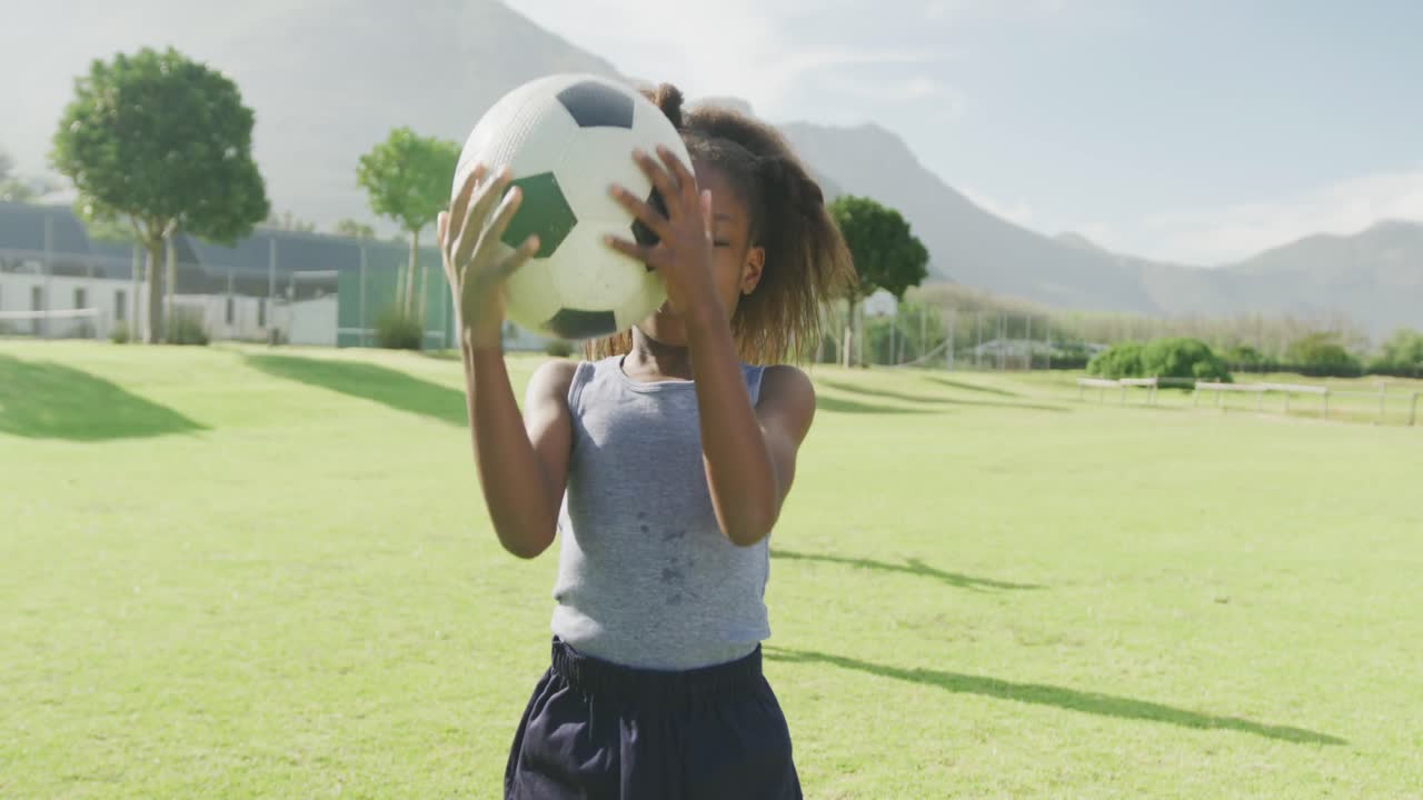 retrato de video de una colegiala afroamericana sonriente sosteniendo un fútbol en el campo