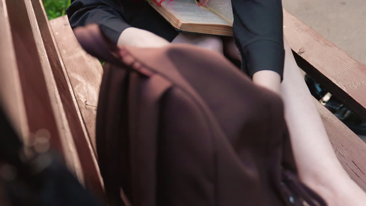 흰색 옷을 입은 여성이 벤치에 앉아 백팩을 메고 휴대폰을 확인하고 있어요. 알록달록한 매니큐어를 칠한 손톱과 맨 다리가 보이고, 편안한 복장을 입고 생각에 잠긴 듯한 분위기이며 조용한 공원 분위기예요. 나무 벤치에 앉아 알림을 확인하고 있습니다.