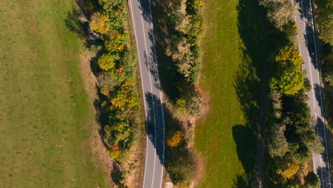 cars travel on curvy winding road in germany autumn countryside - top down aerial