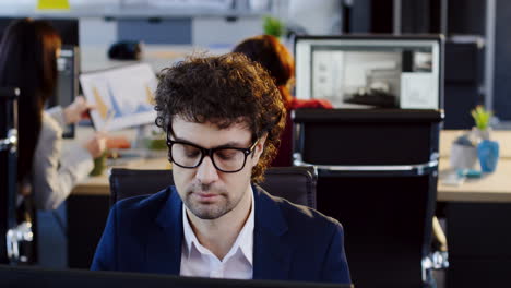 caucasian businessman in glasses working on computer and talking on the phone in the office