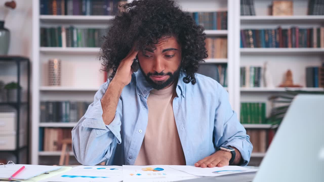 Young arabian man looks at charts and clutches head during financial audit