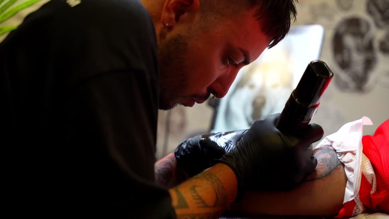 Tattoo artist applies vaseline on the skin of his client and continue painting with ink on her arm