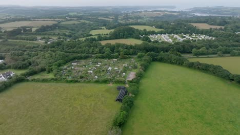 village and hamlet and farmhouse amid rolling green countryside and farmer's fields. with misty coastal inlet in distance. summer, cornwall, uk.