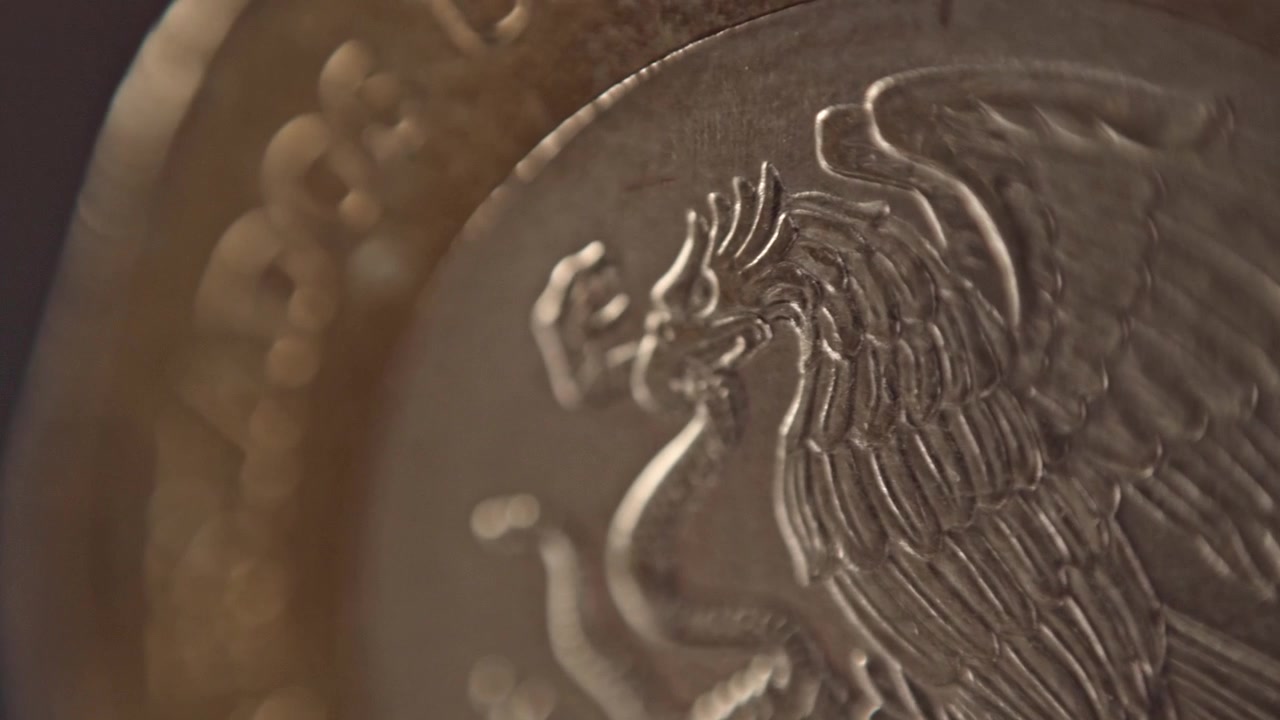 Primo piano macro dello stemma messicano su moneta che mostra l'emblema dell'aquila e del serpente. Dettagli finemente incisi e texture metallica evidenziano il design della valuta nazionale su sfondo sfocato