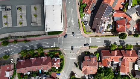 traffic scene on junction of american town in summer. aerial top down rising shot. solar panels on roof of orange tile houses. parking area of shopping center. turning cars on street
