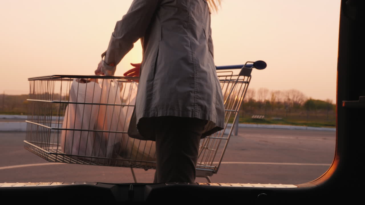 젊은 여자는 쇼핑백을 차 트렁크에 넣는다