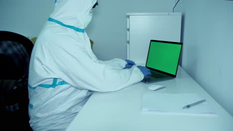 Healthcare-worker-in-PPE-gear-in-white-hospital-room-working-on-green-screen-laptop