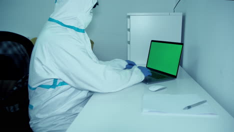 healthcare worker in ppe gear in white hospital room working on green screen laptop