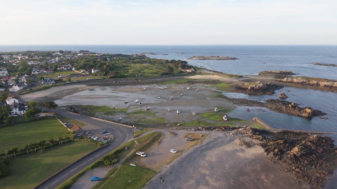 Porto di Bordeaux, Guernsey, Isole del Canale. Riprese aeree con drone in avanti ad alta quota di spiagge tranquille e del vecchio porto sulla costa orientale con la bassa marea, con acqua limpida e calma e viste lontane