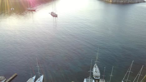 aerial view at the calm bay with yachts in small harbour and on anchor. rising drone shot, panorama of the sea and mountains.sun flare
