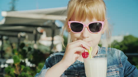 Lustiges-Mädchen-In-Rosa-Gläsern-Trinkt-Einen-Cocktail-Auf-Der-Sommerterrasse-Des-Caférests-Mit-Kindern-Con