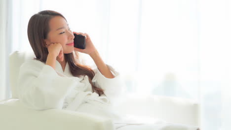 테리 옷을 입은 목욕 가운을 입고 편안한 의자에 앉아 휴대폰으로 이야기하는 예쁜 여성의 클로즈업