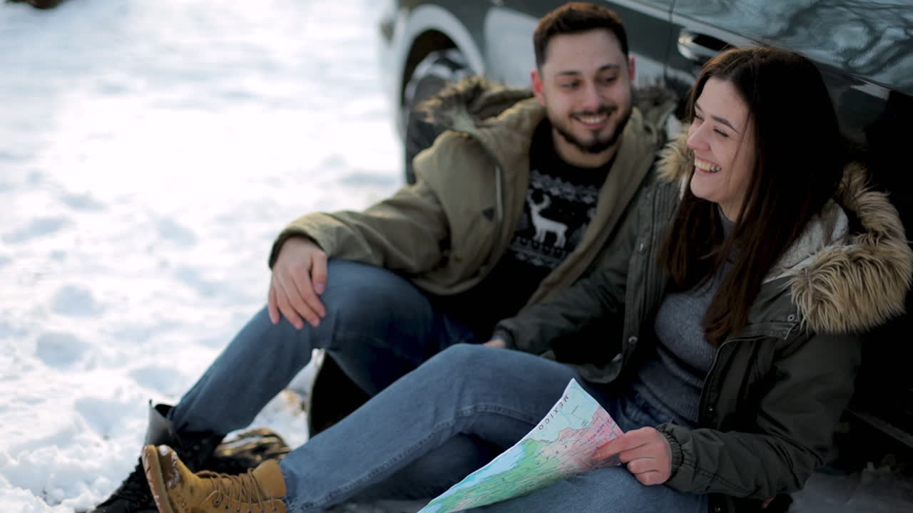 pareja caucásica sentada en la nieve y descansando durante un viaje por carretera.