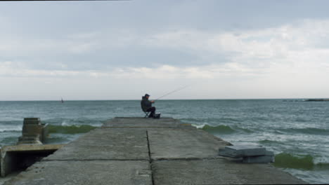 pescador pescando con caña en la construcción de un puente marítimo en la costa de la playa de primavera