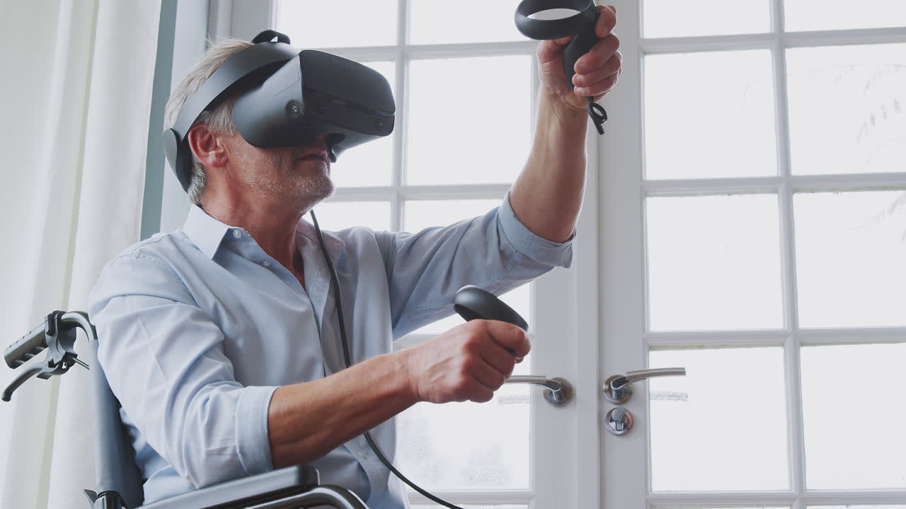 Anziano disabile in sedia a rotelle a casa che indossa un visore per la realtà virtuale e tiene in mano controller di gioco.