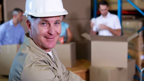 trabajador de almacén apilando cajas y sonriendo a la cámara