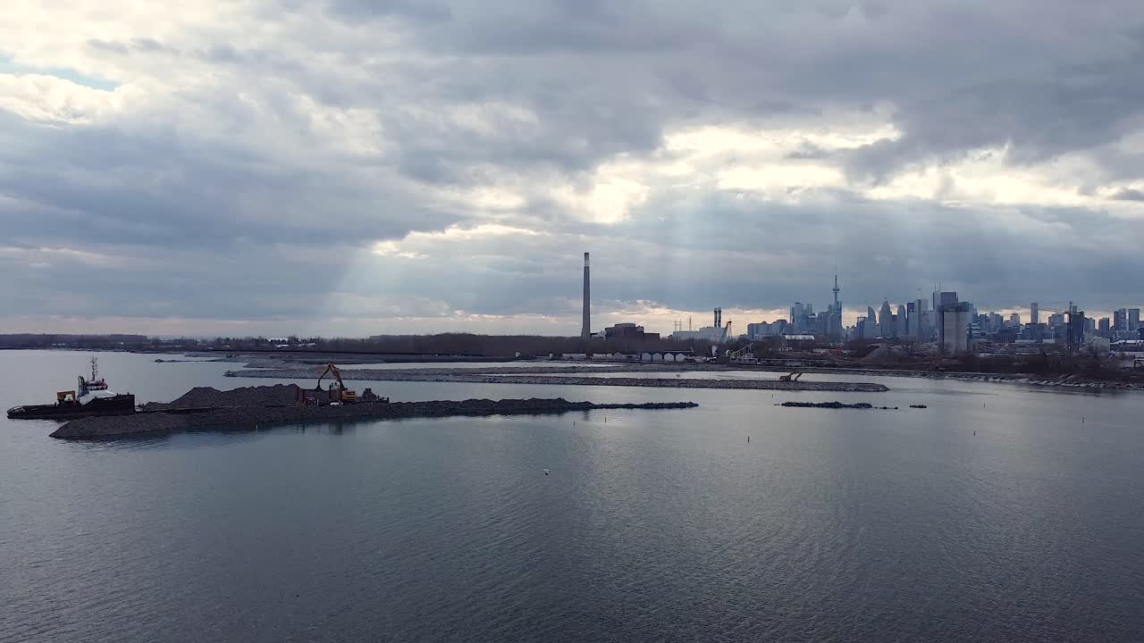 Mezzi pesanti che costruiscono un frangiflutti con rocce vicino al lungomare e allo skyline di Toronto