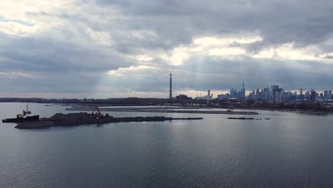 Heavy-equipment-building-breakwater-from-rocks-with-near-waterfront-and-Toronto-skyline