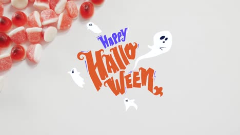 Happy-halloween-text-banner-and-ghosts-icons-against-close-up-of-candy-corns-on-white-surface