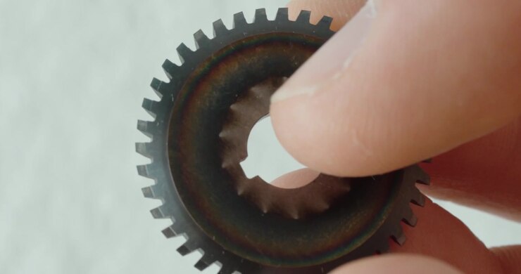 Extreme close-up of a hand holding a small disc milling cutter, showing sharp metal teeth, precision machining, tool inspection, and industrial craftsmanship.