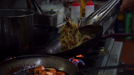 slow motion close up shot capturing chef cooking noodles, flipping, mixing and stirring the ingredients in the frying pan on stovetop